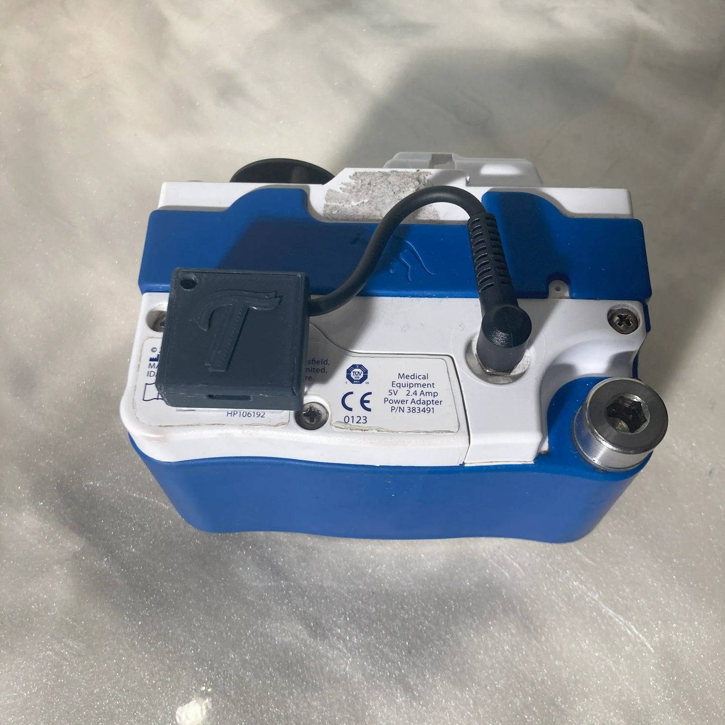 Rear view of a Kangaroo Joey enteral feeding pump with a Tubie Tech USB-C charger mounted to the back using the optional 3M Dual Tack accessory